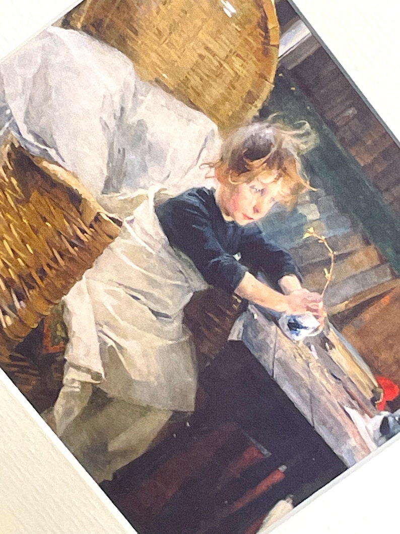 以下が含まれることがあります： 白いドレスと黒いセーターを着た若い女の子が、籐のバスケットに座って、葉のついた小さな枝を持っています。女の子は長い茶色の髪をしていて、枝を見下ろしています。背景は素朴な木製の壁です。