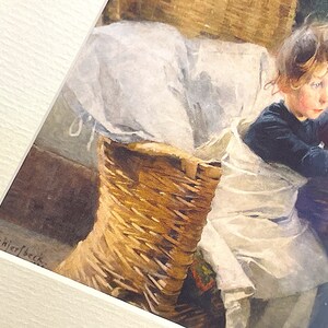 以下が含まれることがあります： 白い布がかけられた籐のバスケットに座っている若い女の子の水彩画。女の子は濃い青色のシャツを着ていて、髪を後ろに結んでいます。絵は「H. Schjerfbeck.」と署名されています。