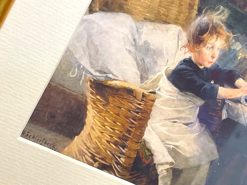 以下が含まれることがあります： 白い布がかけられた籐のバスケットに座っている若い女の子の水彩画。女の子は濃い青色のシャツを着ていて、髪を後ろに結んでいます。絵は「H. Schjerfbeck.」と署名されています。