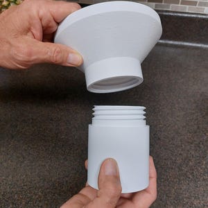 May include: A white, two-piece product, possibly a kitchen or bathroom accessory, is held apart. The top piece is a flared cone shape with small, evenly spaced bumps. The bottom piece is cylindrical with external threads.