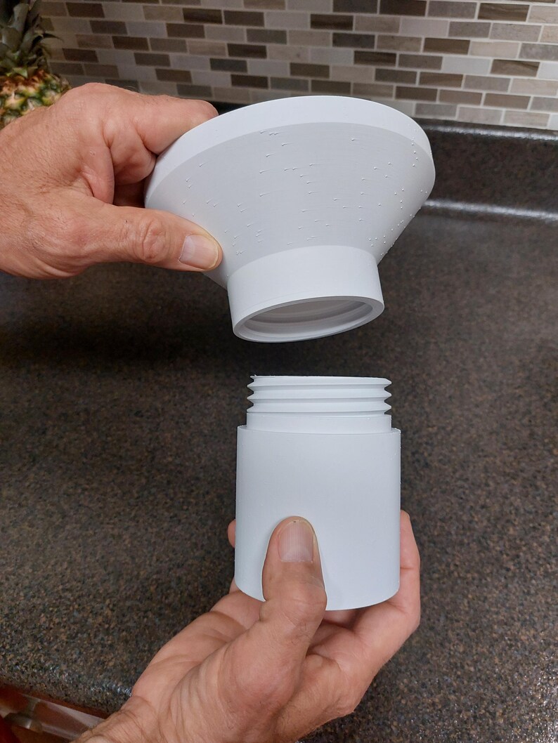 May include: A white, two-piece product, possibly a kitchen or bathroom accessory, is held apart. The top piece is a flared cone shape with small, evenly spaced bumps. The bottom piece is cylindrical with external threads.
