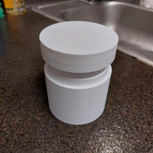 May include: A white, cylindrical object with a flat top and a stacked design. The object is composed of multiple layers, creating a textured appearance. It sits on a dark, speckled countertop.