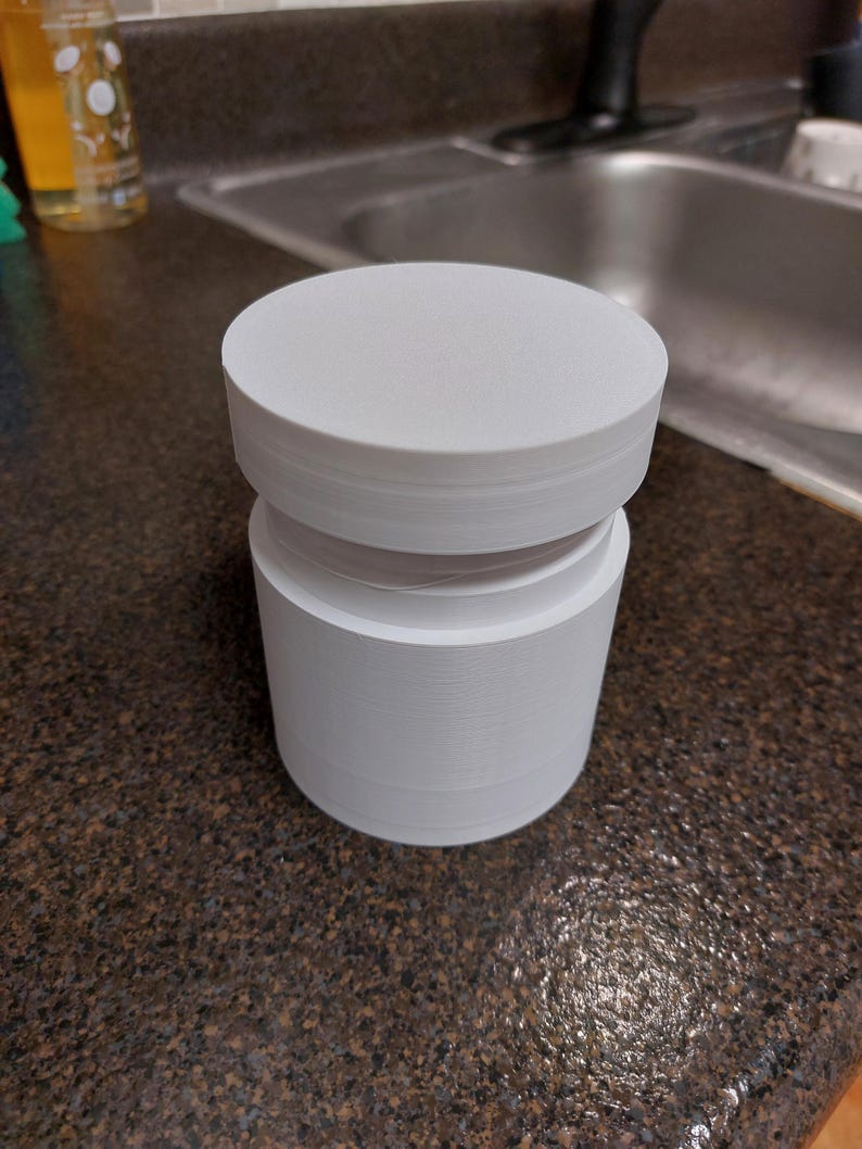 May include: A white, cylindrical object with a flat top and a stacked design. The object is composed of multiple layers, creating a textured appearance. It sits on a dark, speckled countertop.