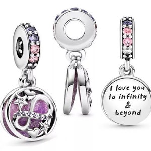 Puede incluir: Encanto de plata con un símbolo de infinito morado y rosa, estrellas y corazones. El encanto es de doble cara y se abre para revelar las palabras "Te amo hasta el infinito y más allá".