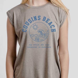 May include: A tan sleeveless t-shirt with the words "COUSINS BEACH" in blue, encircling a sun and wave graphic. Below, the text reads "my whole life was measured in summers."