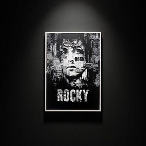 May include: Black and white framed art print featuring a portrait of a person with the word "ROCK" in the image. The word "ROCKY" is printed in bold white letters at the bottom of the image.