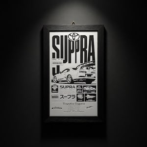 Könnte beinhalten: Schwarz-weiß gerahmtes Poster mit einem Toyota Supra. Das Poster zeigt das Toyota-Logo, das Wort "SUPRA" und technische Details. Das Poster ist an einer dunklen Wand befestigt.