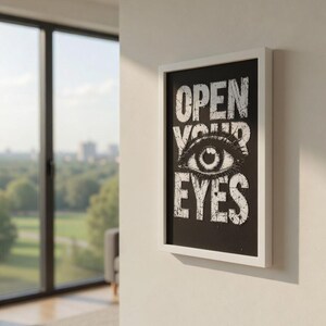 May include: A framed art print with the words "OPEN YOUR EYES" in white, stylized text on a black background. The artwork features a detailed eye illustration. The frame is white, and the print is mounted on a white wall.