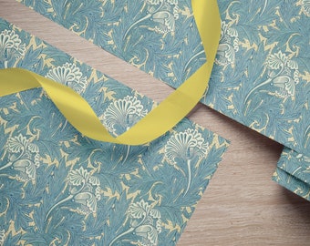 Può includere: Carta da regalo con motivo floreale blu e crema con un nastro giallo. La carta presenta un motivo ripetitivo di fiori e foglie stilizzati.