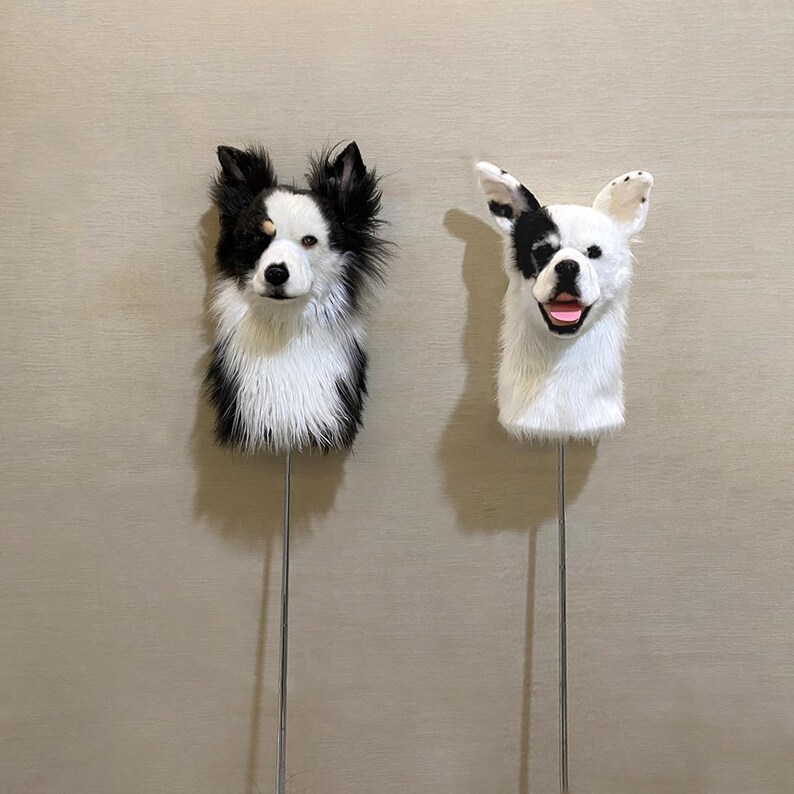 May include: Two black and white dog head sculptures on metal rods. The dog on the left has black fur with white markings and the dog on the right is mostly white with black markings.