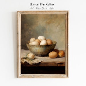 May include: A framed still life print featuring a rustic bowl filled with eggs of varying shades of brown and white. The artwork, labeled "Blossom Print Gallery Printable art," is set against a muted, neutral background, evoking a vintage aesthetic.