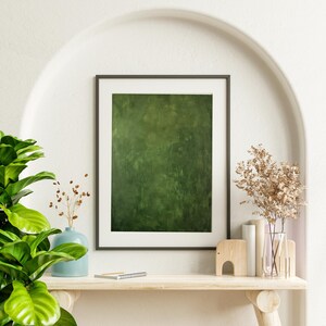 May include: A framed abstract art print with a textured green background. The artwork is displayed on a wooden shelf with decorative items, including a blue vase, dried flowers, and a wooden elephant figurine. The setting is a white alcove.