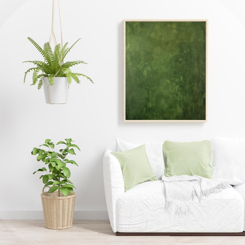 May include: A living room scene featuring a white sofa with light green pillows and a framed abstract green painting. A hanging fern in a white pot and a potted plant in a wicker basket add a touch of nature.
