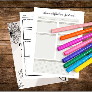 May include: A stack of white paper journals with the text "Theme Reflection Journal" and colorful markers. The journals have sections for theme, date, and reflection prompts. Markers are pink, orange, purple, blue, green, and yellow.