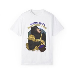 May include: White t-shirt featuring a cartoon bear in a yellow dress holding a basket of berries. The bear is set against a green and blue background, with the text "Momma Bear's Berry Pickin' Patch" in yellow and blue.