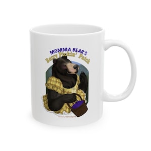 May include: White ceramic mug featuring a cartoon bear in a yellow dress holding a basket of berries. The mug has the text "Momma Bear's Berry Pickin' Patch" in blue and yellow. A whimsical design for a kitchen or gift.