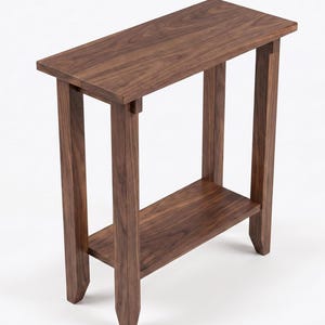 May include: A narrow rectangular console table crafted from dark brown wood with a visible grain pattern. The table features a flat top surface, four straight legs with pointed feet, and a lower shelf positioned between the legs for storage.