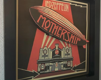 May include: A framed print of a Led Zeppelin album cover featuring a red and black airship with the text "Mothership" and "Led Zeppelin" in white. The airship is flying over a red and black building with the words "Rock" and "Roll" on the sides.