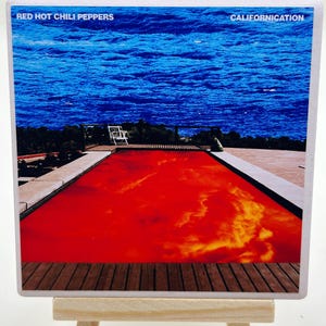 May include: A rectangular image featuring the album art for Red Hot Chili Peppers' "Californication." The artwork depicts a red pool against a blue ocean backdrop. The band's name and album title are printed at the top.