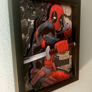 May include: A framed 3D pop art print of Deadpool, a superhero character, holding a sword and a gun. The print is set against a comic book background with speech bubbles that read "You told me I shouldn't take these..." and "So much I forgot your name. I'm so old and I just take pity on you. You're practically a baby. You're a baby!"