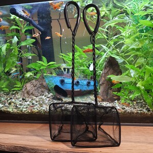 May include: Two black metal fish nets with black mesh. The nets are hanging from a blue and white boat-shaped object. The boat is sitting on a bed of gravel and rocks.