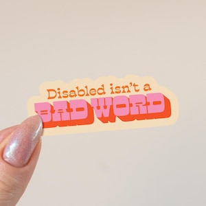 Peut inclure: Un autocollant avec le texte "Disabled isn't a bad word" en orange et rose dans une police rétro. L'autocollant a un fond crème et est tenu par une main avec un ongle scintillant.