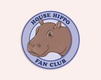 May include: A circular sticker featuring a brown hippopotamus head illustration centered within a light blue border. The text HOUSE HIPPO is arched across the top and FAN CLUB is arched across the bottom in dark blue capital letters.