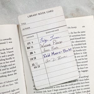 Peut inclure: Une carte de bibliothèque vintage avec des inscriptions manuscrites, partiellement superposée aux pages d'un livre ouvert. La carte indique les noms des emprunteurs et les dates de retour, évoquant la nostalgie. Les pages du livre sont visibles.