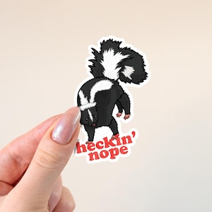 Peut inclure: Autocollant représentant un putois de dessin animé noir et blanc avec une queue touffue. Le putois est en position défensive, avec le texte "heckin' nope" en rouge.