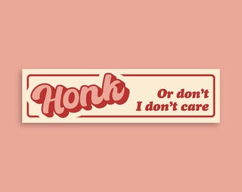 May include: A rectangular bumper sticker with the word "Honk" in a retro font, with a red outline and a light pink fill. The text "Or don't, I don't care" is to the right in a smaller font. The background is a light peach color.