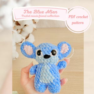 Peut inclure: Un jouet amigurumi en crochet bleu ressemblant à Stitch du film Lilo & Stitch. Le jouet a de grands yeux noirs, un nez rose et des oreilles roses. Le texte "The Blue Alien Pocket movie friend collection PDF crochet pattern" est visible sur l'image.