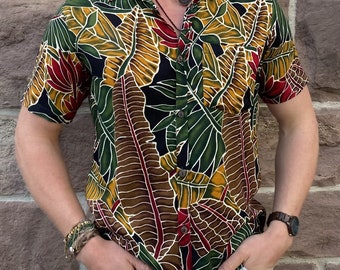 May include: A short-sleeved button-down shirt with a tropical leaf print in shades of green, brown, yellow, and red. The shirt has a black background and a relaxed fit.