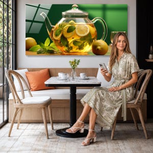 May include: A rectangular glass wall art piece featuring a clear glass teapot filled with golden tea, sliced lemons, and fresh green mint leaves. The background is a solid deep green, and the composition includes two whole lemons on the surface.
