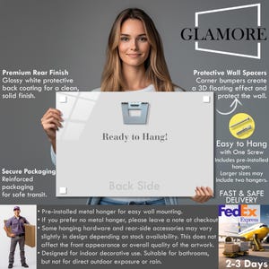 The image is a promotional advertisement featuring a woman holding a sign that says "Ready to Hang!" The sign is for a product called "Glamore" that is described as a premium rear finish, protective wall spacer, and easy to hang with one screw. The ad also highlights the product's features such as secure packaging, a back side, and a pre-installed metal hanger for wall mounting.