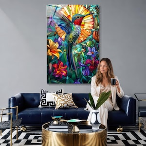 May include: A vertical wall art piece featuring a vibrant stained glass style illustration of a hummingbird in flight, surrounded by colorful lilies and a large circular sun motif in shades of orange, yellow, blue, red, and purple.
