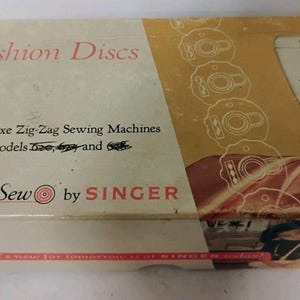 May include: A rectangular cardboard box for Singer Touch & Sew Fashion Discs. The box is cream and gold with red text reading Fashion Discs for Deluxe Zig-Zag Sewing Machines. It features an illustration of a sewing machine and a person sewing.