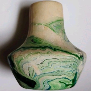 May include: A small vase with a wide, rounded base and a narrow neck, featuring a marbled pattern of cream, light green, and dark green swirls throughout the exterior surface, creating a fluid, layered appearance across the entire object.