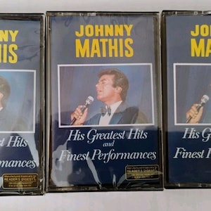 May include: Three vintage cassette tapes of Johnny Mathis's "His Greatest Hits and Finest Performances." Each tape features a portrait of Mathis and text in yellow and white on a dark blue background.