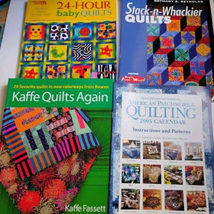 May include: Four quilting books and a calendar titled 24-Hour Baby Quilts, Stack-n-Whackier Quilts, Kaffe Quilts Again, and American Patchwork & Quilting 2005 Calendar. The covers feature colorful quilt patterns, floral designs, and geometric shapes.