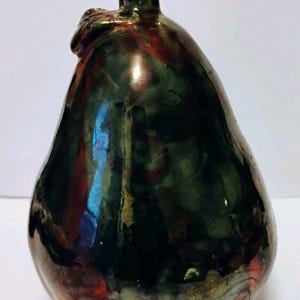 Puede incluir: Una escultura de cerámica en forma de pera con un esmalte brillante multicolor. Los colores incluyen verde oscuro, rojo y toques de azul y dorado. La escultura tiene un pequeño tallo y una superficie texturizada.