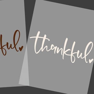 May include: Two rectangular sheets featuring the word thankful in a cursive script font. One sheet displays the text in a dark brown color, while the other sheet displays the text in a white color. Each word includes a small heart icon.