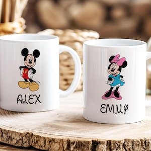 Puede incluir: Dos tazas de cer&aacute;mica blanca con ilustraciones de Mickey y Minnie Mouse. Mickey lleva pantalones cortos rojos y zapatos amarillos, Minnie un vestido azul y zapatos rosas. Las tazas tienen los nombres "ALEX" y "EMILY".