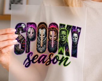以下が含まれることがあります： 透明な正方形の転写シート。太字でカラフルなフォントで「SPOOKY season」という文字が描かれています。文字の中には、マスクを被った人物やモンスターなど、様々なホラー映画のキャラクターの精巧で鮮やかなイラストが描かれています。