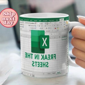 K&ouml;nnte beinhalten: Wei&szlig;e Keramiktasse mit einem gr&uuml;nen und wei&szlig;en Microsoft Excel-Tabellenblatt-Design. Die Tasse tr&auml;gt den Text "SHEETS IN THE FREAK", der darauf gedruckt ist.