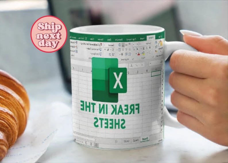 K&ouml;nnte beinhalten: Wei&szlig;e Keramiktasse mit einem gr&uuml;nen und wei&szlig;en Microsoft Excel-Tabellenblatt-Design. Die Tasse tr&auml;gt den Text "SHEETS IN THE FREAK", der darauf gedruckt ist.