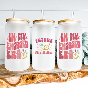 May include: Three frosted glass tumblers with bamboo lids and straws. The tumblers feature pink and white text that says "In My Engaged Era" and "Future Mrs. Miller" with gold ring and diamond illustrations.