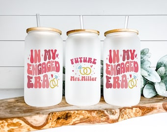 May include: Three frosted glass tumblers with bamboo lids and straws. The tumblers feature pink and white text that says "In My Engaged Era" and "Future Mrs. Miller" with gold ring and diamond illustrations.