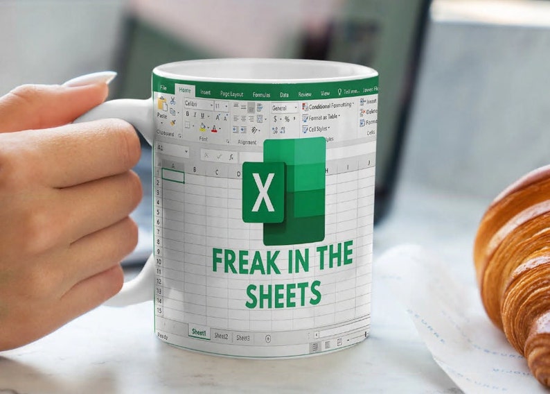 K&ouml;nnte beinhalten: Eine wei&szlig;e Kaffeetasse mit einem gr&uuml;nen Microsoft Excel-Tabellenblatt-Design. Die Tabelle zeigt den Text "FREAK IN THE SHEETS".