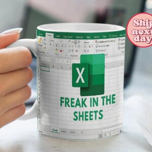 K&ouml;nnte beinhalten: Eine wei&szlig;e Keramiktasse mit einem gr&uuml;nen und wei&szlig;en Microsoft Excel-Tabellenblattdesign. Die Tasse zeigt das Excel-Logo und den Text "Freak in the Sheets".