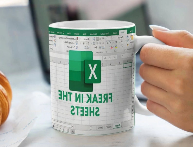 K&ouml;nnte beinhalten: Wei&szlig;e Keramiktasse mit einem gr&uuml;n-wei&szlig;en Microsoft Excel-Logo und dem aufgedruckten Text "FREAK IN THE SHEETS".